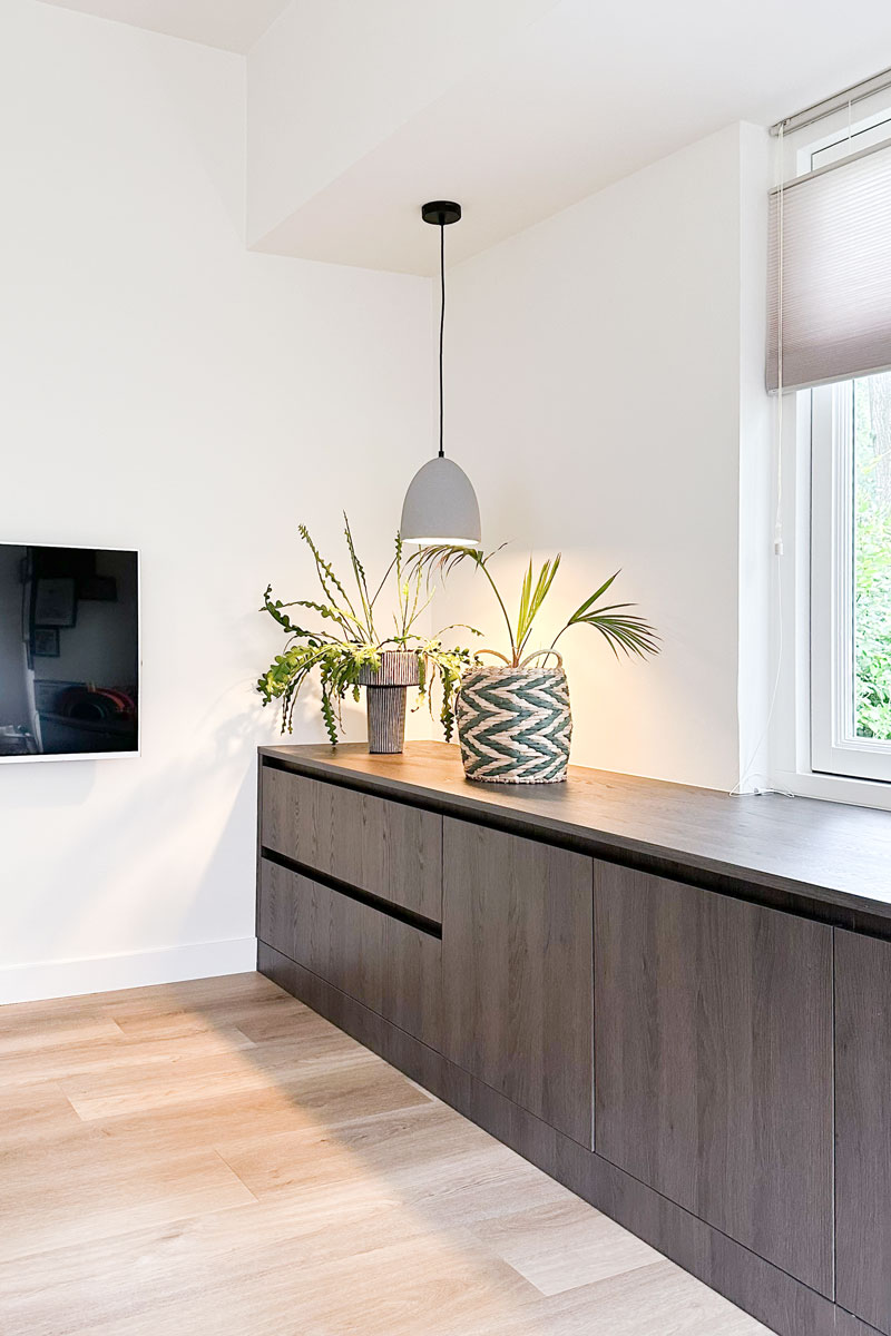 Donkere houten kast in jaren 30 woning met hanglamp en groene planten.